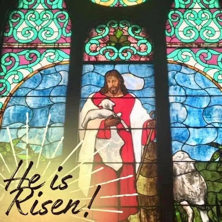 Our Good Shepherd stained-glass window: Jesus carrying a lamb, with the words &ldquo;He is Risen!&rdquo;